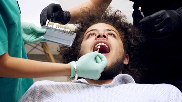 Footage of a dentist with her assistant checking a young man´s shade of tooth color视频素材