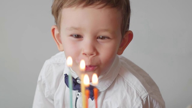 可爱的男孩在彩虹生日蛋糕上吹蜡烛视频素材