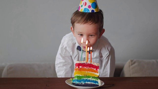 可爱的男孩在彩虹生日蛋糕上吹蜡烛视频素材