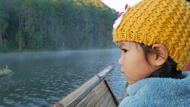 一个可爱的小女孩在竹筏上通过雾漂浮在湖面上在早上，在泰国Mae Hong Son视频素材