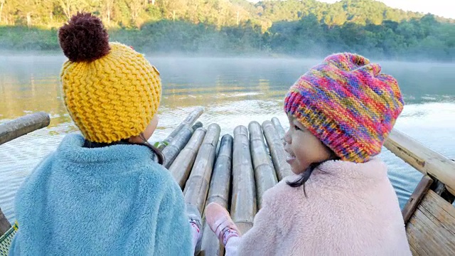 可爱的小女孩一起在竹筏上玩，穿过雾浮在湖面上，在早上的泰国，美宏森视频素材