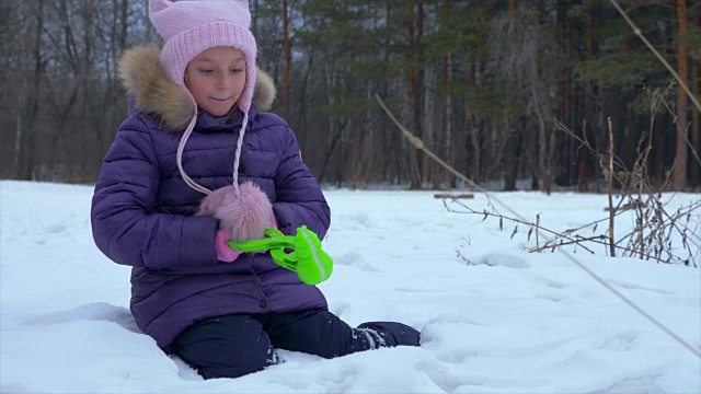 冬天的森林里，女孩坐在雪地上堆雪人视频素材