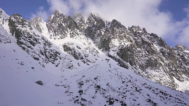 在寒冷的阳光明媚的天气里，滑雪游览覆盖在雪中的岩石山脉景观视频素材