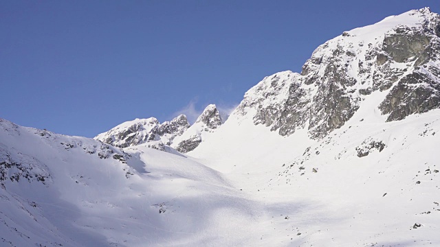 在寒冷的阳光明媚的天气里，滑雪游览覆盖在雪中的岩石山脉景观视频素材