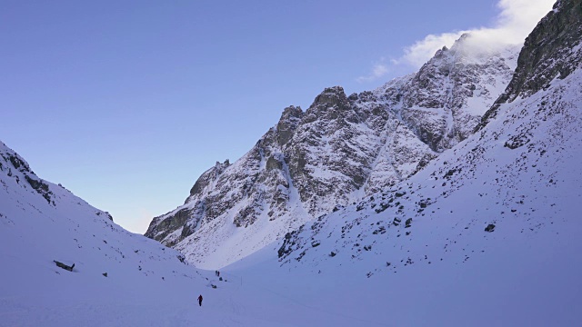 在寒冷的阳光明媚的天气里，滑雪游览覆盖在雪中的岩石山脉景观视频素材