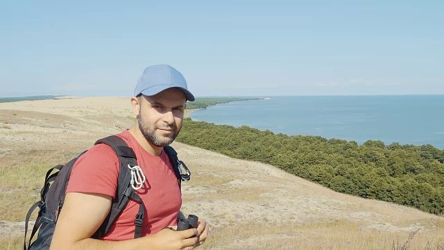 用双筒望远镜观察野生动物的旅行者。男人们在度假中观赏自然景观。一个背包旅行者正在用双筒望远镜看大海，看美丽的风景。山。海滩。视频素材