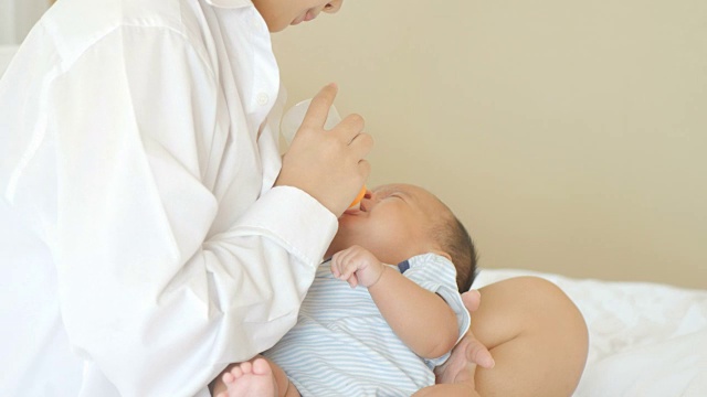 年轻的亚洲母亲在家用奶瓶喂男婴。视频素材