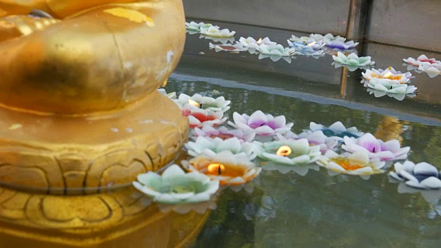 镀金的佛像周围漂浮着莲花形状的多色蜡烛视频素材