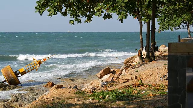 美丽的海景。海浪拍打着石滩，上面放着弃置的黄色浮标，还有一棵树。风景如画的风景视频素材