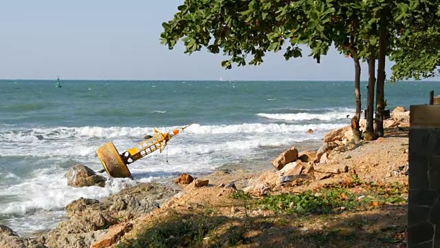 美丽的海景。海浪拍打着石滩，上面放着弃置的黄色浮标，还有一棵树。风景如画的风景视频素材