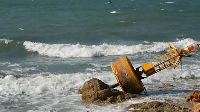 湛蓝的海岸上的黄色大浮标。海浪拍打着浮标和岸边的大岩石视频素材