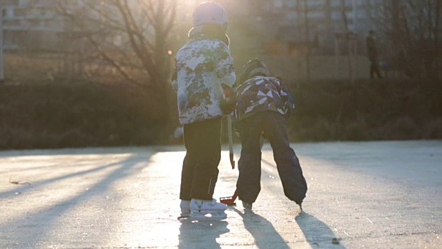 孩子们、男孩们、朋友们和兄弟们在公园里冰冻的湖面上打曲棍球和滑冰，冬天的日落时分视频素材