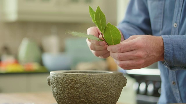 雄将月桂叶加入研钵中，用杵研磨视频素材