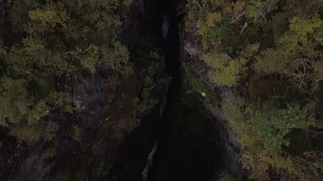 4K鸟瞰图瀑布通过深山谷的岩石和森林，快速倾斜视频素材