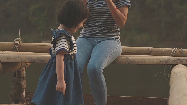 一个女人和一个小女孩坐在山河边视频素材