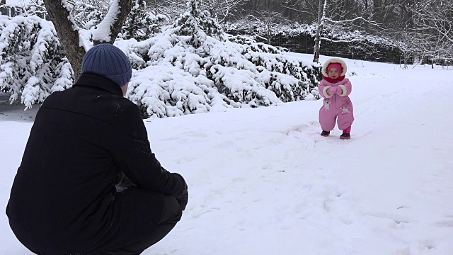 在寒冷的冬天，爸爸和宝宝在白雪覆盖的公园里玩耍。FullHD视频素材