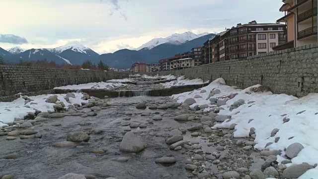 在保加利亚班斯科，一架无人机低空飞过冬季河流，背景是皮林山脉视频素材