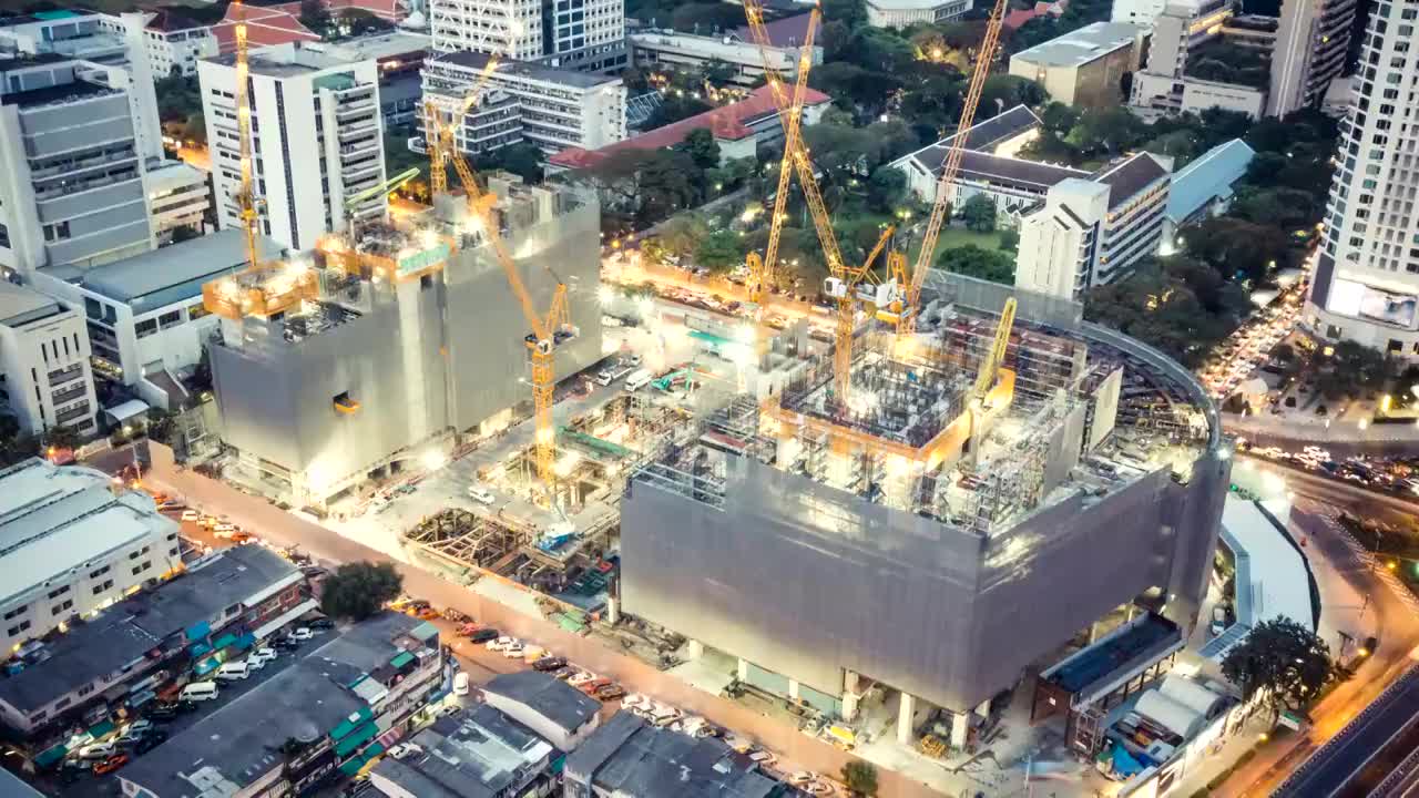 延时拍摄的建筑工地，在夜晚有城市交通的灯光轨迹，俯视图。先进的建筑技术，繁忙的地铁市中心城市景观，或发展中的工业国家概念视频素材