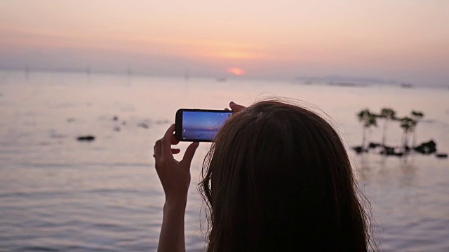 一个女人用她的智能手机在美丽的日落海滩附近的海边度假。1920 x1080慢动作视频素材