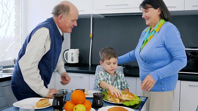 退休老人夫妇拥抱孩子在午餐时间在厨房旁边的桌子上美味的食物视频素材