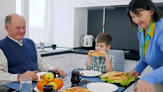 老人的家庭早餐，奶奶端来了美味的包子放在盘子里，孙子和爷爷坐在桌边视频素材