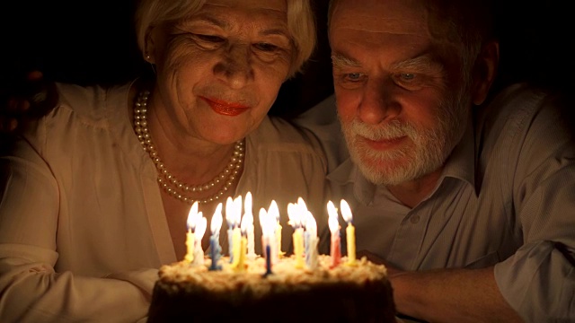 相爱的老年夫妇晚上在家用蛋糕庆祝结婚纪念日。吹灭蜡烛视频素材