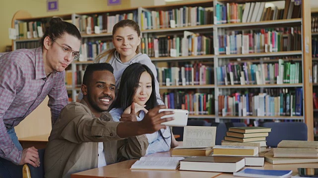 一群留学生在大学图书馆用智能手机自拍，开心地微笑着。快乐的朋友在准备考试时休息视频素材