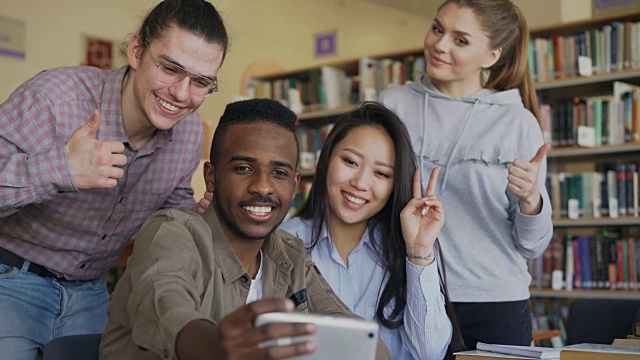 一群留学生在大学图书馆用智能手机自拍，开心地微笑着。快乐的朋友们在一起准备项目的同时休息视频素材