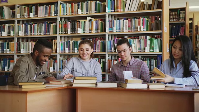 多民族学生聊天和准备考试，而坐在大学图书馆的桌子视频素材