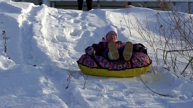 慢动作:女孩在雪橇上滚动在一个滑管上跑。孩子们喜欢在冬天下坡。视频素材