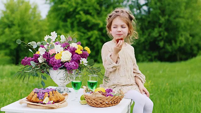 可爱的小女孩穿着漂亮的裙子坐在桌子上吃着巧克力糖果。圣帕特里克节野餐视频素材