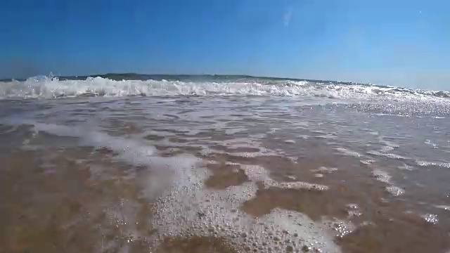 在一个阳光明媚的夏日，在美丽的沙滩上，海浪盖住了相机。从低角度拍摄动作摄影机。视频素材