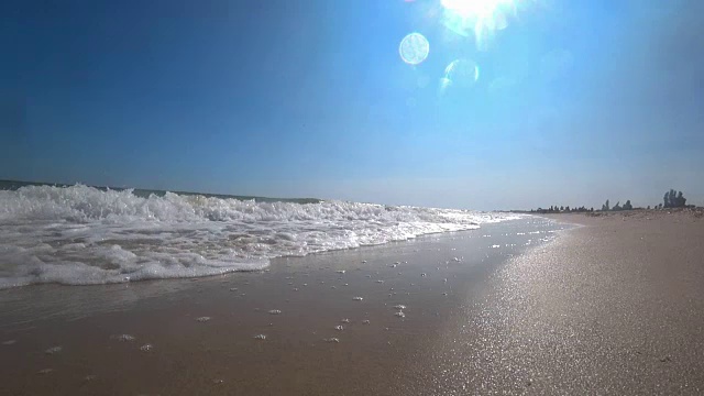 在一个阳光明媚的夏日，在美丽的沙滩上，海浪盖住了相机。从低角度，慢动作拍摄动作摄像机。视频素材