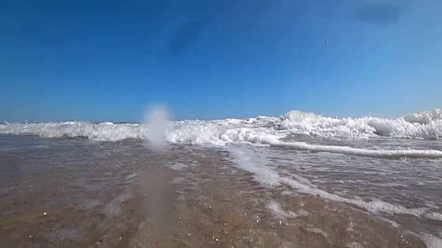 在一个阳光明媚的夏日，在美丽的沙滩上，海浪盖住了相机。从低角度，慢动作拍摄动作摄像机。视频素材