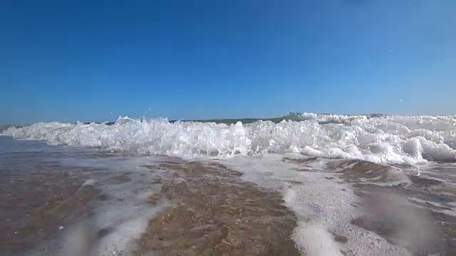 在一个阳光明媚的夏日，在美丽的沙滩上，海浪盖住了相机。从低角度，慢动作拍摄动作摄像机。视频素材