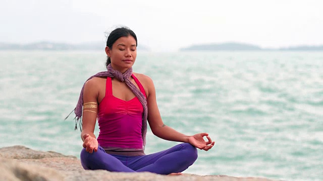 亚洲女人在瑜伽莲花姿势在石质海滩沉思视频素材