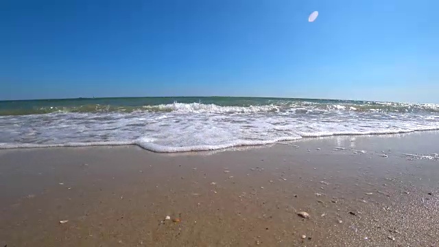 在一个阳光明媚的夏日，美丽的沙滩上，海浪盖住了相机。从低角度拍摄动作摄影机。视频素材