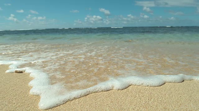 慢镜头，特写:阳光明媚的日子里，充满异国情调的海滩正被泡沫的海浪冲刷着。视频素材