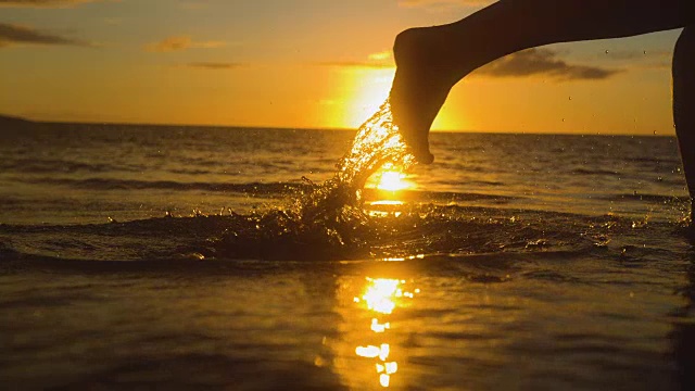 特写:无忧无虑的女人在金色的夕阳下赤脚在浅海中奔跑。视频素材