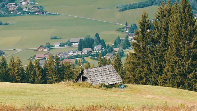 舒适的非常古老的木屋在奥地利阿尔卑斯山的一个小山上，绿色的草在新的现代房子的背景，古老的乡村木屋在村庄视频素材