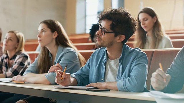 西班牙裔青年在他的同学在教室里。年轻聪明的人在大学学习期间听讲座并做笔记。视频素材