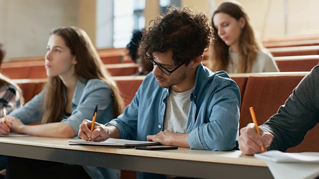 西班牙裔青年在他的同学在教室里。年轻聪明的人在大学学习期间听讲座并做笔记。视频素材