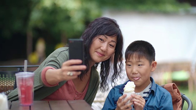 妈妈和孩子在户外咖啡馆用智能手机拍照视频素材