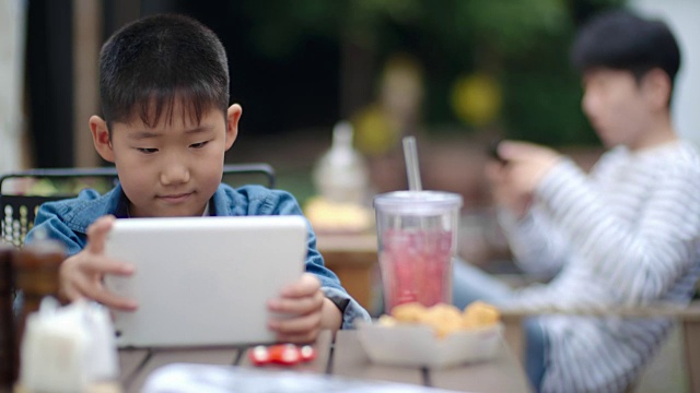 可爱的亚洲男孩在户外咖啡馆玩数字平板电脑视频素材