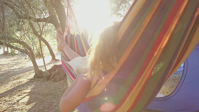 在阳光明媚的夏日露营地，女人在吊床上放松，摇摆视频素材