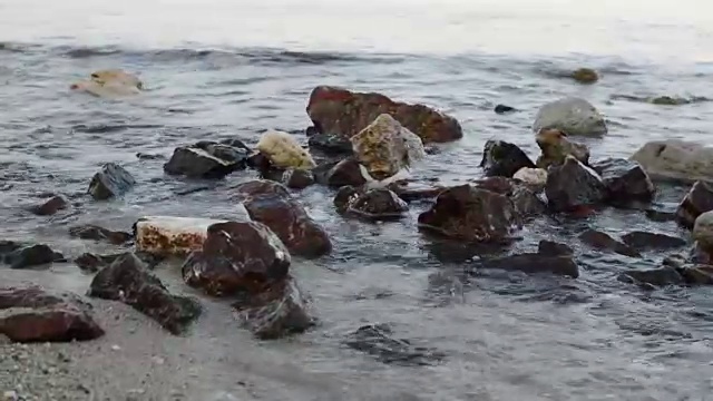 小波浪在白色沙滩岸边的岩石上的特写视频素材