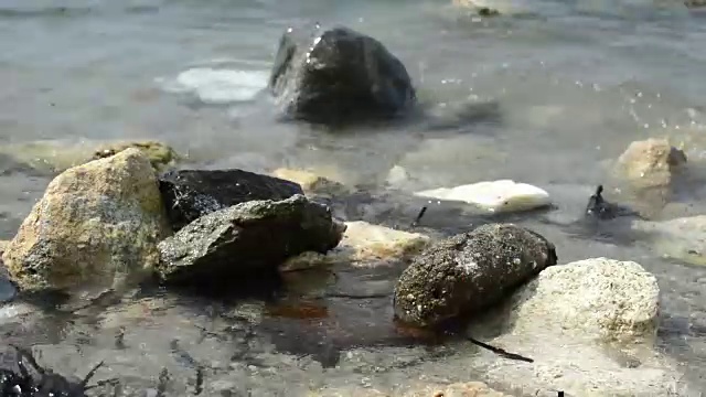 小波浪在白色沙滩岸边的岩石上的特写视频素材