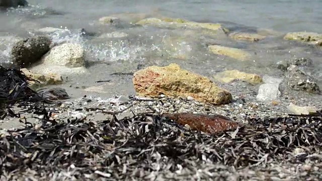 小波浪在白色沙滩岸边的岩石上的特写视频素材