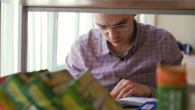 年轻英俊的白人男学生戴着眼镜站在书架前拿着书翻页寻找信息视频素材