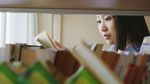 美丽的亚洲认真的女学生站在书架附近的书籍在大图书馆拿着教科书翻页阅读视频素材